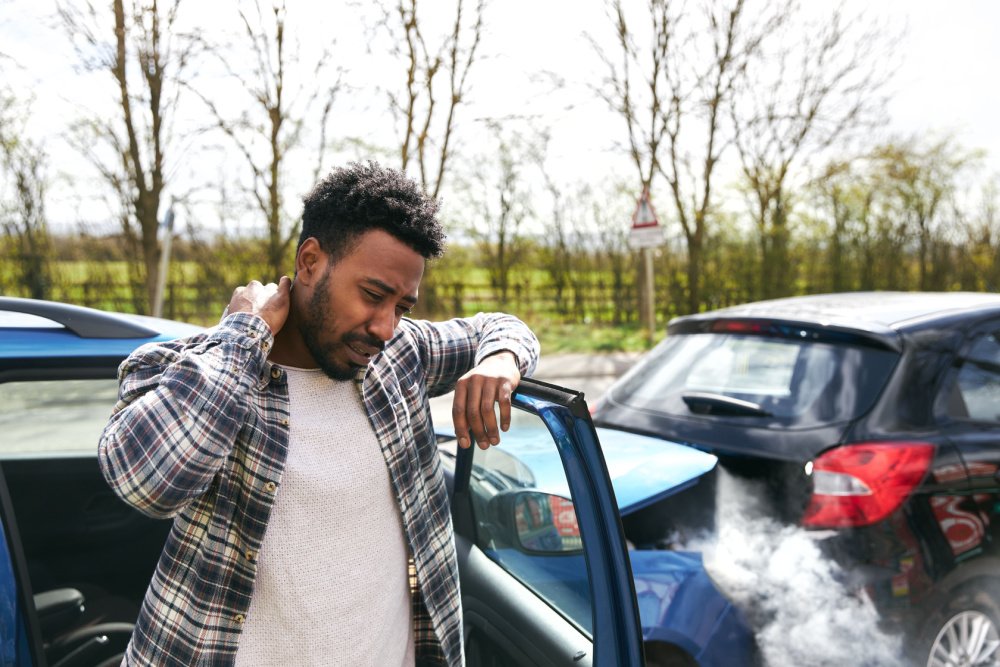 male driver rubbing neck in pain from whiplash injury standing by damaged car after traffic accident